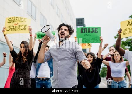 Mann schreit durch Megaphon, während er mit Menschen auf der Straße protestiert In der Stadt Stockfoto