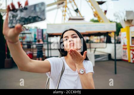 Junge Frau weht Kuss während der Aufnahme Selfie im Vergnügungspark Stockfoto