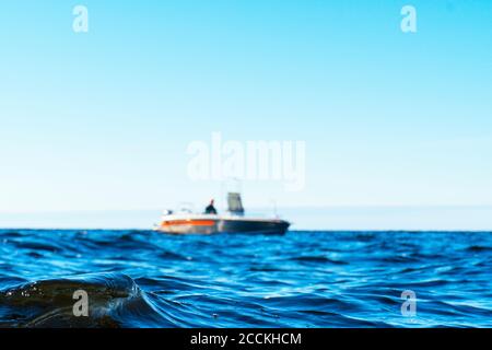 Wasseroberfläche mit verschwommenem Fischer auf dem Boot im blauen Ozean. Schöne Seeufer mit dem verschwommenen Fischerboot. Angeln Motorboot mit Angler. Meer se Stockfoto