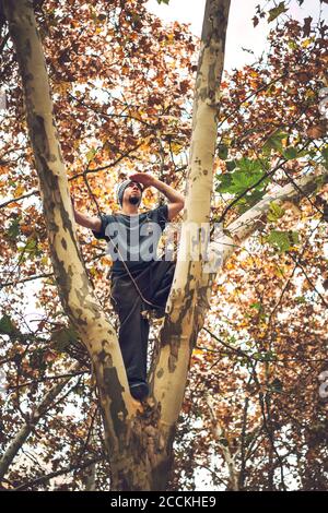 Low-Angle-Ansicht des jungen Mannes, der im Stehen wegschaut Auf Baumstamm Stockfoto
