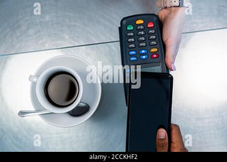 Der Kunde, der kontaktlos über das Smartphone im Café bezahlt Stockfoto