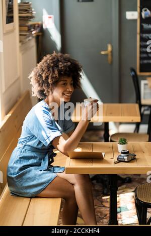 Nachdenkliche Frau hält Kaffeebecher, während sie am Tisch sitzt Café Stockfoto