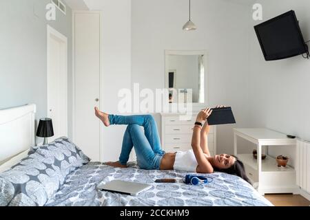 Lächelnde Frau mittleren Erwachsenen hält Buch, während sie sich auf dem Bett ausruhen Zu Hause Stockfoto
