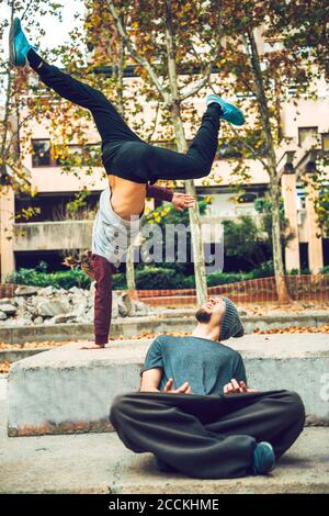 Junger Mann, der einen Freund beim Handstand im öffentlichen Park ansieht Stockfoto