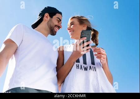 Lächelnde Frau hält Smartphone Blick auf Freund gegen klar Blauer Himmel Stockfoto