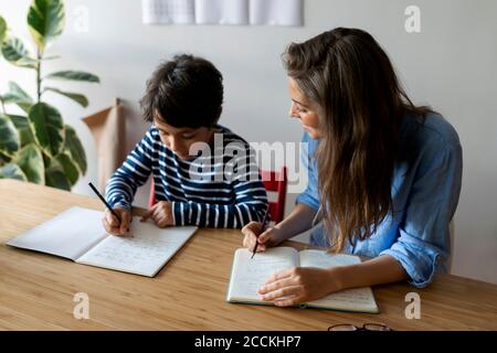 Junge Frau sitzt mit Student Hausaufgaben auf dem Tisch zu tun Zu Hause Stockfoto