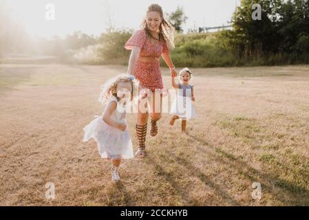 Glückliche Mutter läuft mit Töchtern auf einer Wiese im Gegenlicht Stockfoto