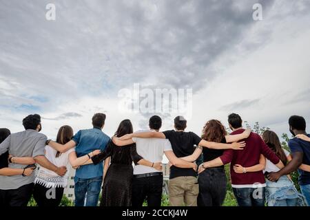 Rückansicht von weiblichen und männlichen Freunden mit den Armen Stehen gegen bewölkten Himmel Stockfoto