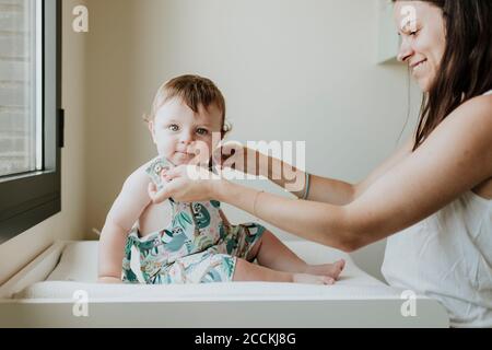 Mutter trägt Kleid zu niedlichen Baby Tochter sitzen auf dem Tisch Zu Hause Stockfoto