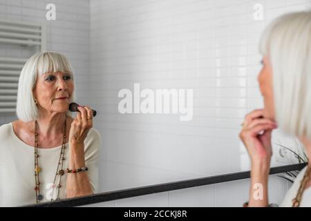 Ältere Frau, die Make-up aufführt, während sie zu Hause im Spiegel schaut Stockfoto