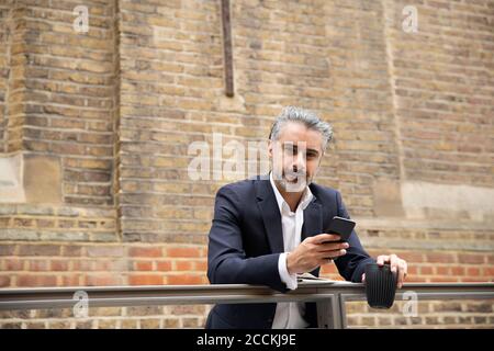 Selbstbewusster Geschäftsmann mit Smartphone gegen die Wand Stockfoto