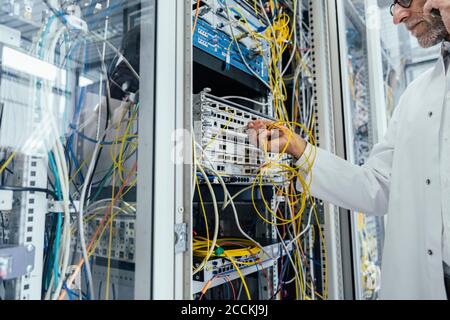 Ein reifer Mann schließt den Transceiver an ein Glasfaserkabel an Rechenzentrum Stockfoto