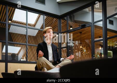 Geschäftsfrau meditiert während sie Yoga am Tisch im Coworking Büro praktiziert Platz Stockfoto