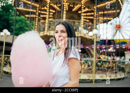 Fröhliche junge Frau mit Zuckerwatte im Vergnügungspark Stockfoto
