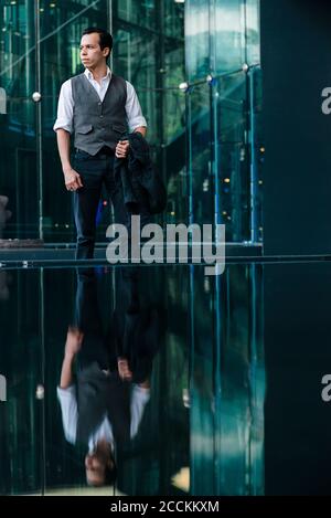 Geschäftsmann, der vor dem Bürogebäude steht und auf Glas reflektiert Stadt Stockfoto