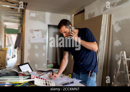 Mann am Telefon, der am Bauplan arbeitet Stockfoto