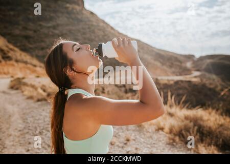 Sportlerin trinkt Wasser aus einer Flasche in den Bergen