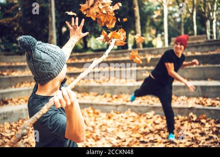 Junge männliche Freunde spielen mit Herbstblättern im öffentlichen Park Stockfoto
