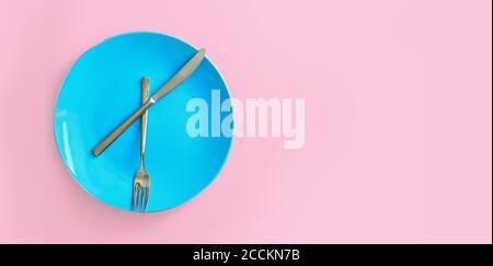 Blaue Platte und rostfreies Messer und Gabel auf rosafarbenem Hintergrund reinigen. Serviertes Besteck. Zeit zu essen Konzept. Speicherplatz kopieren Stockfoto