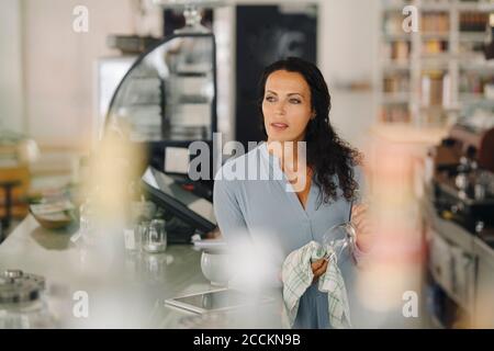 Nachdenkliche Besitzerin putzt Weinglas, während sie auf die Theke schaut Im Café Stockfoto