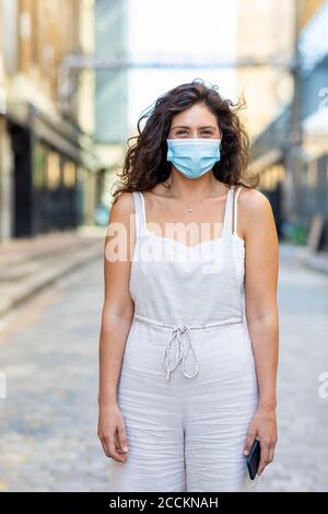 Junge Frau mit Maske auf der Straße in der Stadt stehen Stockfoto