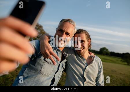 Glücklicher Vater mit erwachsenen Sohn nimmt ein Selfie auf einem Wiese auf dem Land Stockfoto