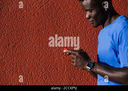 Junger Mann mit Smartphone an der roten Wand in der Stadt An sonnigen Tagen Stockfoto