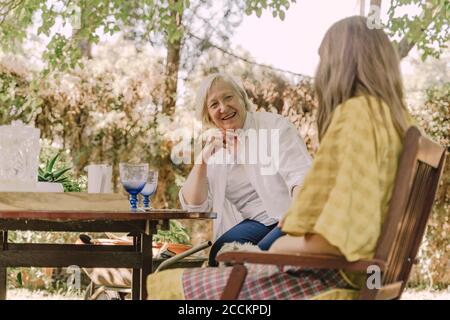 Glückliche ältere Frau im Gespräch mit Tochter, während sie am Tisch sitzt Im Hof Stockfoto