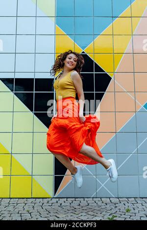 Junge Frau springt vor der bunten Fliesenwand Stockfoto