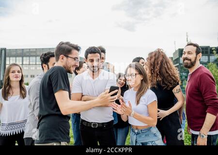 Glücklicher Mann, der Freunden im Park Smartphone zeigt Stockfoto