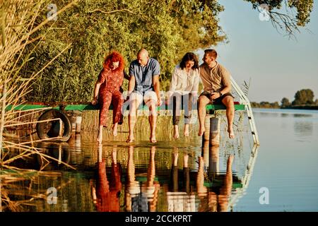 Freunde reflektierten sich im Wasser, das auf dem Steg an einem See saß Stockfoto