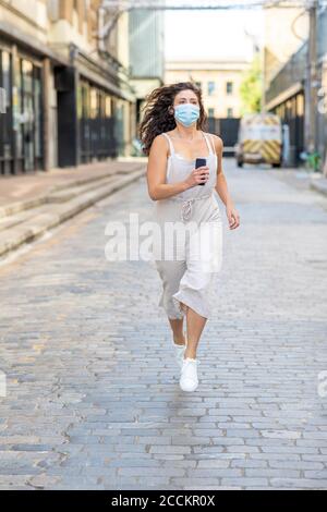 Junge Frau trägt Maske läuft auf der Straße in der Stadt Stockfoto