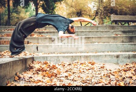 Junger Mann, der im öffentlichen Park über Herbstblätter springt Stockfoto