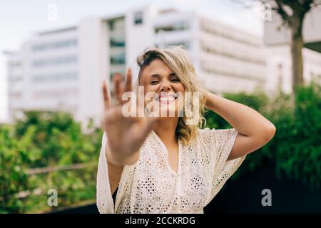 Lächelnde junge Frau mit Hand im Haar zeigt Stop-Geste Stockfoto