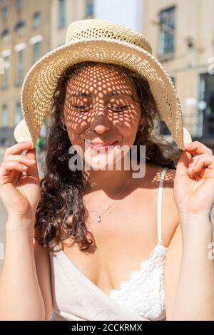 Nahaufnahme einer lächelnden schönen Frau mit geschlossenen Augen und Hut In der Stadt an sonnigen Tag Stockfoto