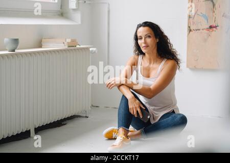 Selbstbewusste Frau mittleren Erwachsenen hält Smartphone auf dem Boden sitzen In Loft-Wohnung Stockfoto
