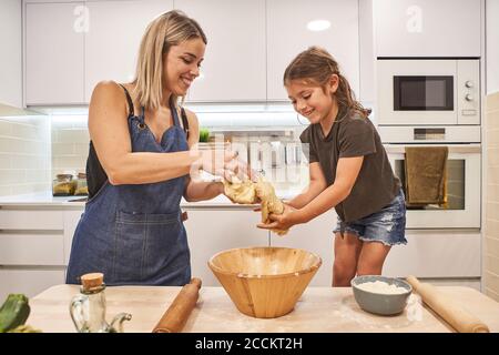 Lächelnde Mutter und Tochter kneten Pizzateig in der Küche Zu Hause Stockfoto