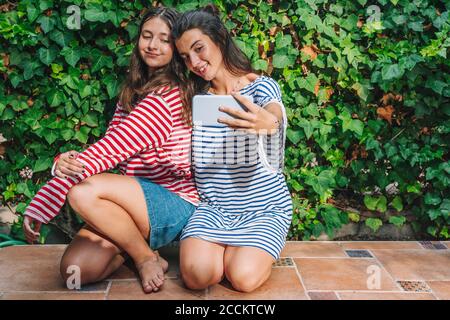 Lächelnde Schwestern, die Selfie über das Smartphone im Hinterhof machen Stockfoto