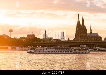 Deutschland, Nordrhein-Westfalen, Köln, untergehende Sonne beleuchtet Tourboot nähert sich Deutz Hängebrücke Stockfoto