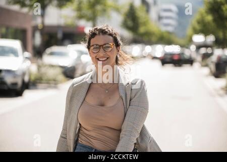 Smiling young woman wearing eyeglasses standing on street in city Stock Photo