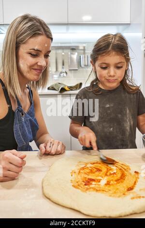 Mutter schaut auf Tochter, die Pizza auf dem Tisch in der Küche zubereitet Stockfoto