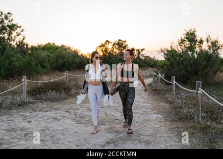 Sportlerinnen tragen Yogamatten beim Wandern auf Sandweg Stockfoto