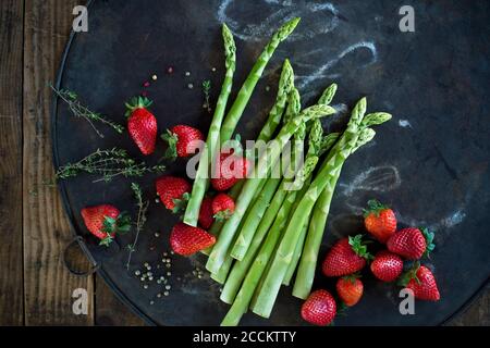 Thymian, Pfefferkorn, Spargelstiele und frische Erdbeeren auf rustikalem Backblech Stockfoto