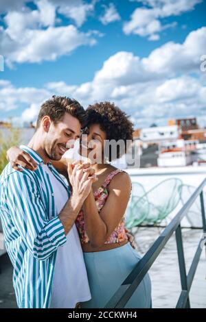 Fröhliches multiethnisches Paar, das auf der Penthouse-Terrasse tanzt Stockfoto