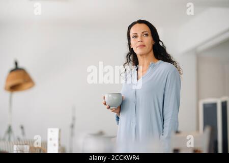 Nachdenkliche Besitzerin hält Kaffeebecher, während sie im Café steht Stockfoto