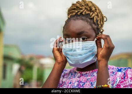 Junge afroamerikanische Frau, die eine schützende Gesichtsmaske aufsetzt Während der COVID-19-Pandemie Stockfoto