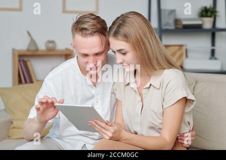 Zeitgenössische junge heterosexuelle Paar mit Tablet, während auf der Couch sitzen Stockfoto