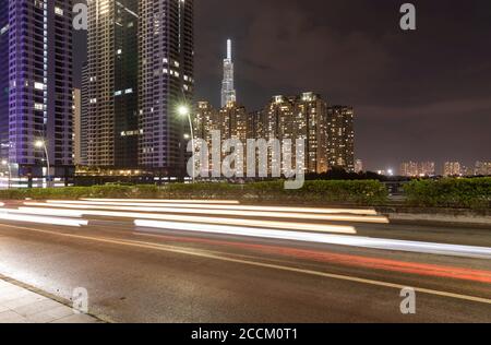 Nächtliche lange Exposition des vorbeifahrenden Verkehrs, der leichte Wege verlässt In einer belebten Straße mit ultramoderner Hochhausarchitektur Der Hintergrund Stockfoto