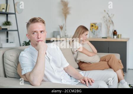 Junger beleidigter oder verärgerter Mann, der auf der Couch saß und dabei ignorierte Seine unglückliche Frau Stockfoto