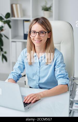 Junge erfolgreiche Geschäftsfrau mit blonden Haaren und toothy Lächeln suchen Bei Ihnen Stockfoto